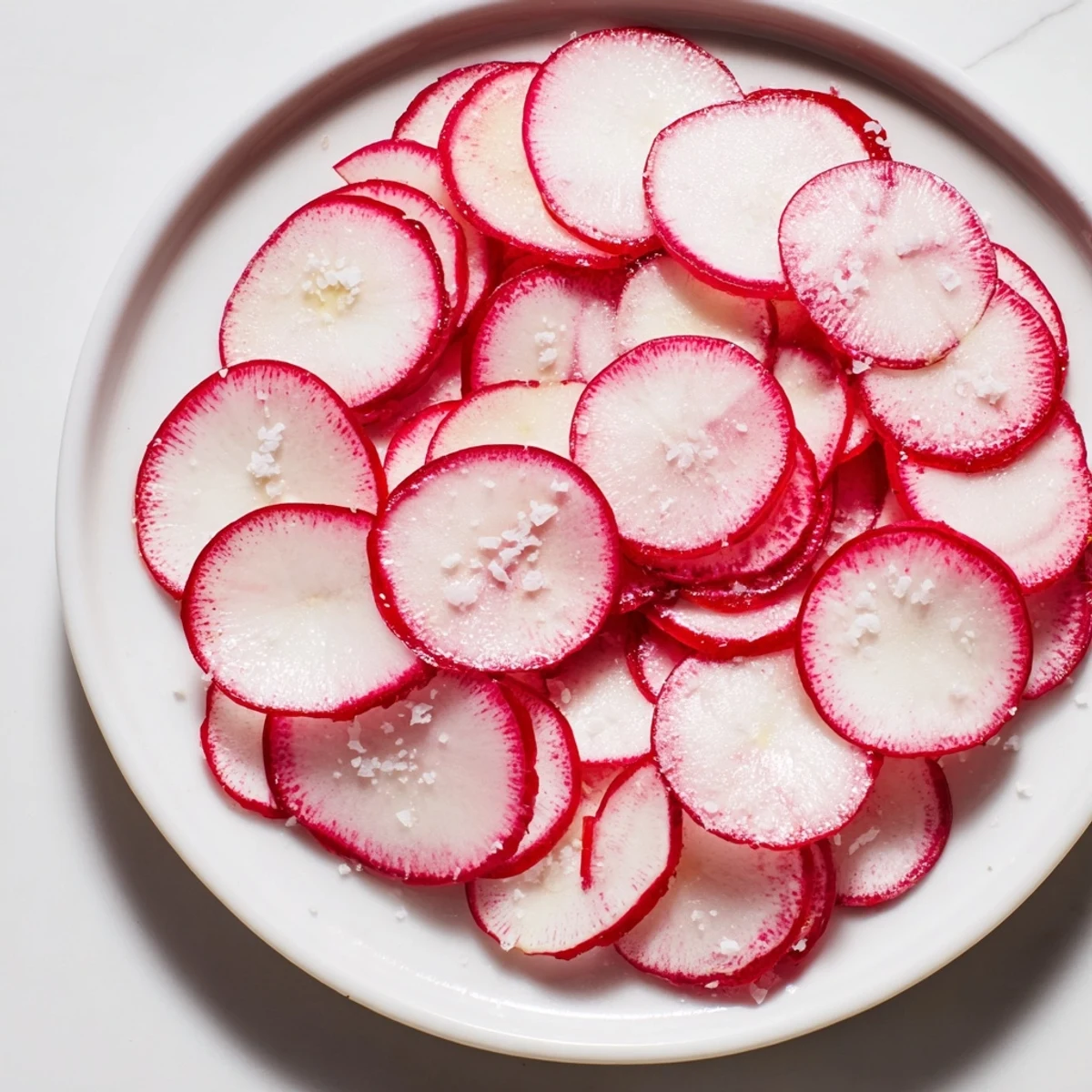 Thin, vibrant red radish slices sprinkled with sea salt, offering a refreshing, crunchy bite.