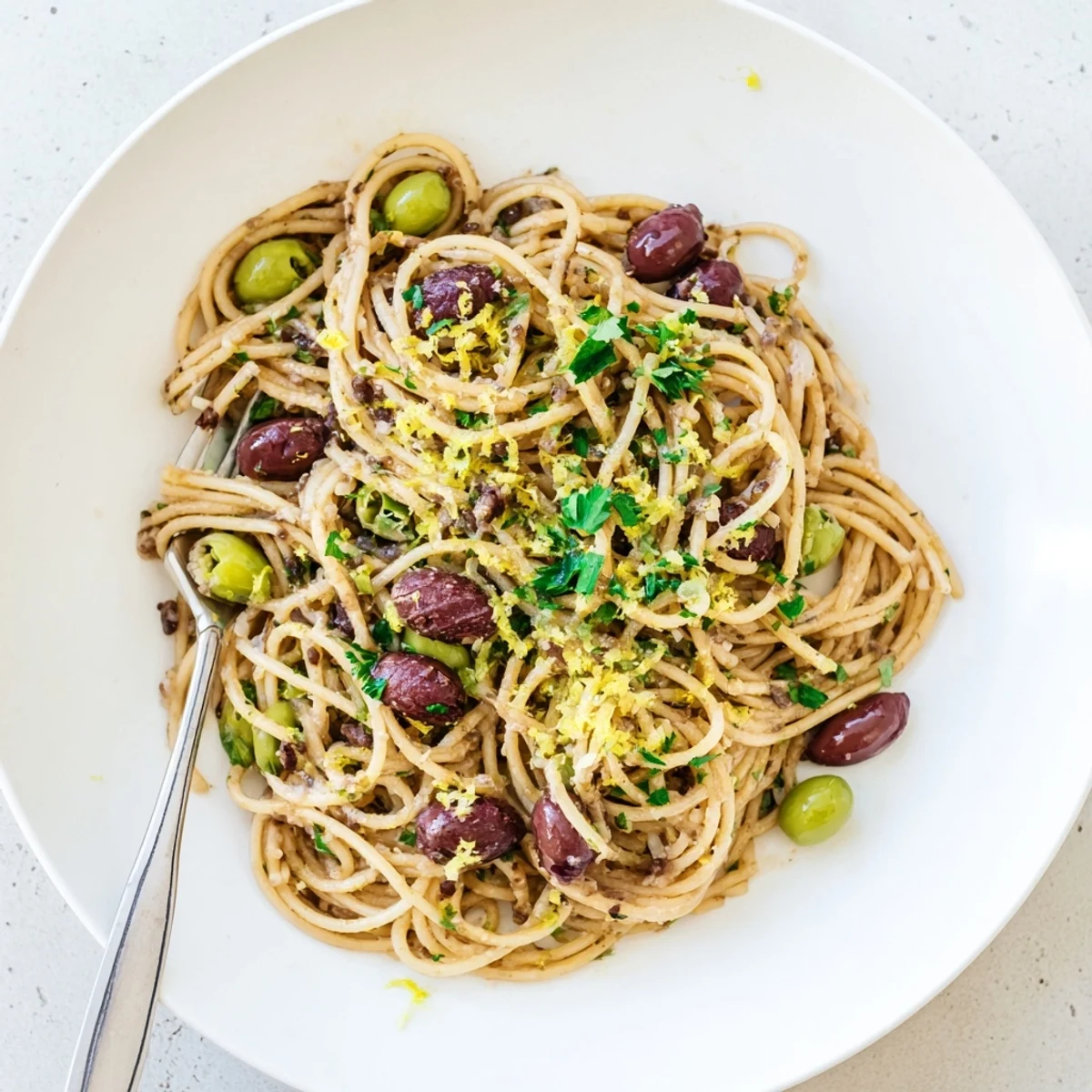 A serving of Olive Tapenade Pasta twirled on a fork, with a side of crusty bread ready to mop up the savory Mediterranean-inspired sauce.
