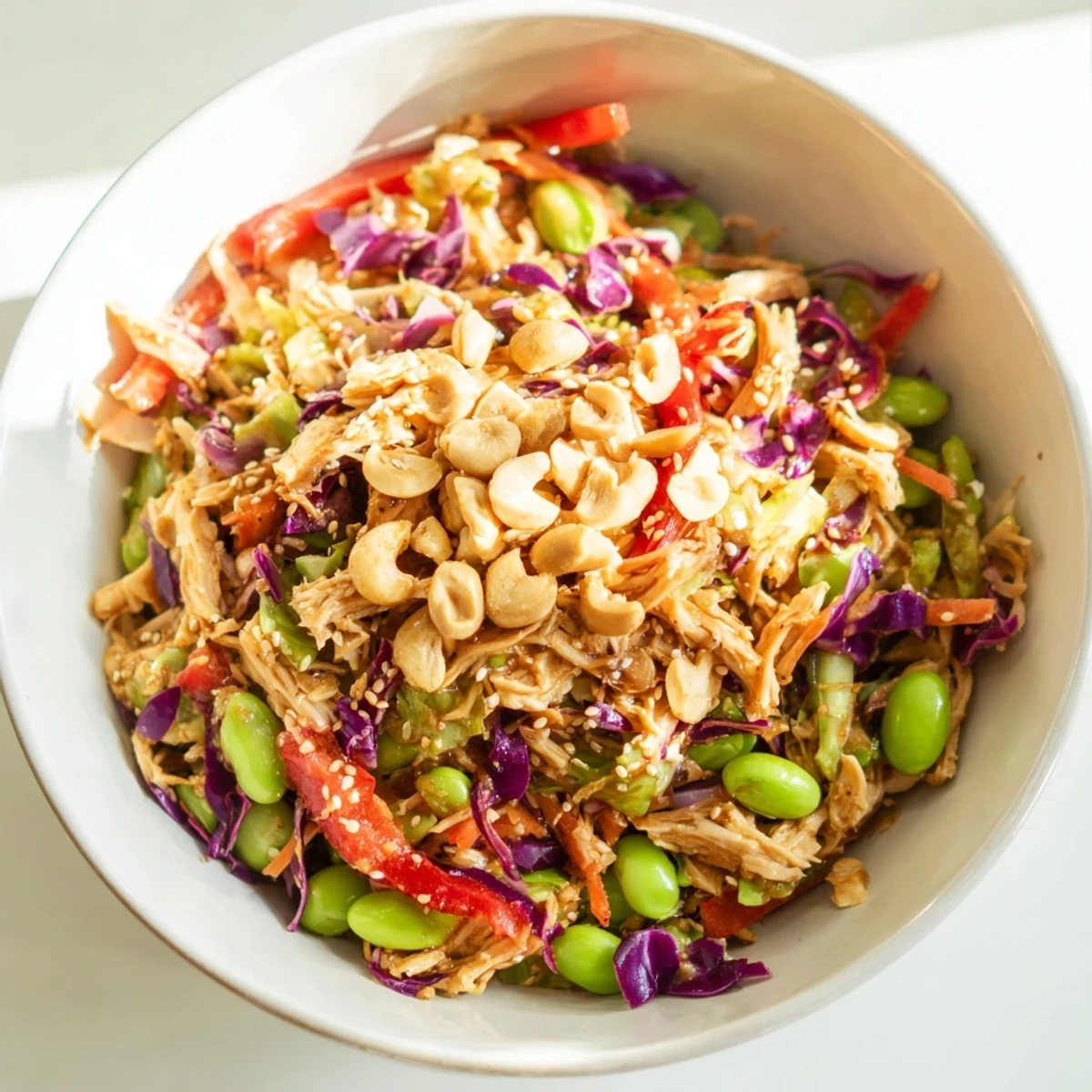 Close-up of Edamame Crunch Chicken Salad in a white bowl, topped with toasted sesame seeds and roasted cashews for added texture and crunch.