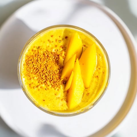 Vibrant overhead shot of a creamy mango turmeric smoothie, garnished with fresh mango slices.