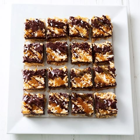 Close-up of baked 7-Layer Magic Bars glistening with a salted caramel drizzle, ready to eat.
