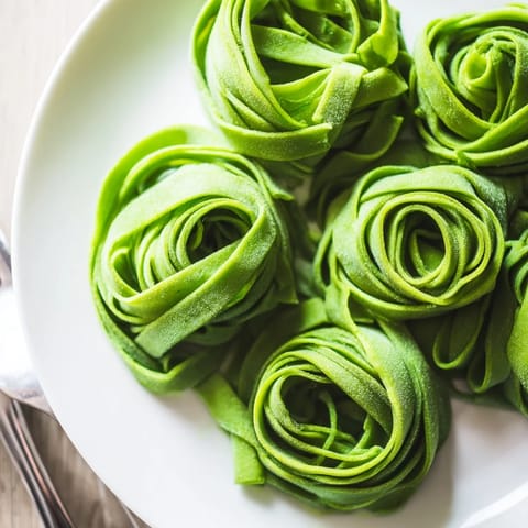 Close-up of tender spinach pasta dough being cut into delicate strips, ready to be boiled for a fresh Italian meal.  
