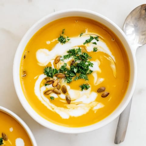 Creamy butternut squash and apple soup ladled into a white bowl, with fresh parsley and a sprinkle of nutmeg.