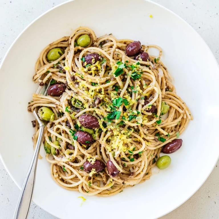 A serving of Olive Tapenade Pasta twirled on a fork, with a side of crusty bread ready to mop up the savory Mediterranean-inspired sauce.