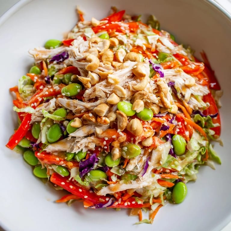 A vibrant, protein-packed Edamame Crunch Chicken Salad garnished with green onions and red bell pepper, served on a light wooden table.